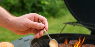 Osoba przygotowująca domowego burgera na grillu, polewająca kotlet kremowym sosem Big Mac w ogrodzie wiosną